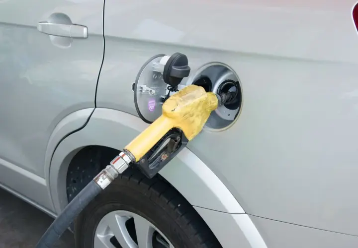 Żółta dysza dystrybutora paliwa wlewana jest do baku srebrnego samochodu. Prosty sposób, jak zatankować auto.
