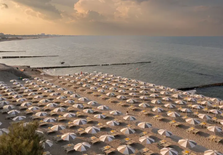 Filetto di ombrelloni e lettini sulla sabbia dorata, con il mare calmo e il cielo crepuscolare a fare da sfondo. Un'immagine che evoca la tranquillità dei **Marche mare**.