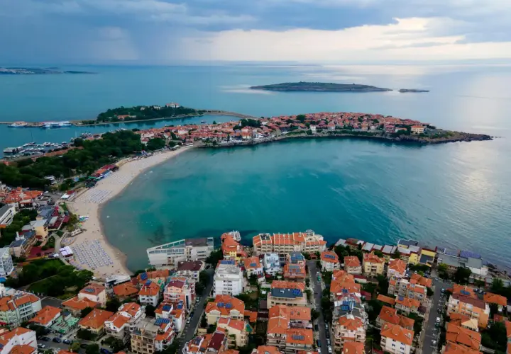 Malownicze wybrzeże podczas wycieczki do Bułgarii. Widok z lotu ptaka na miasteczko z czerwonymi dachami, plażę i turkusowe morze.