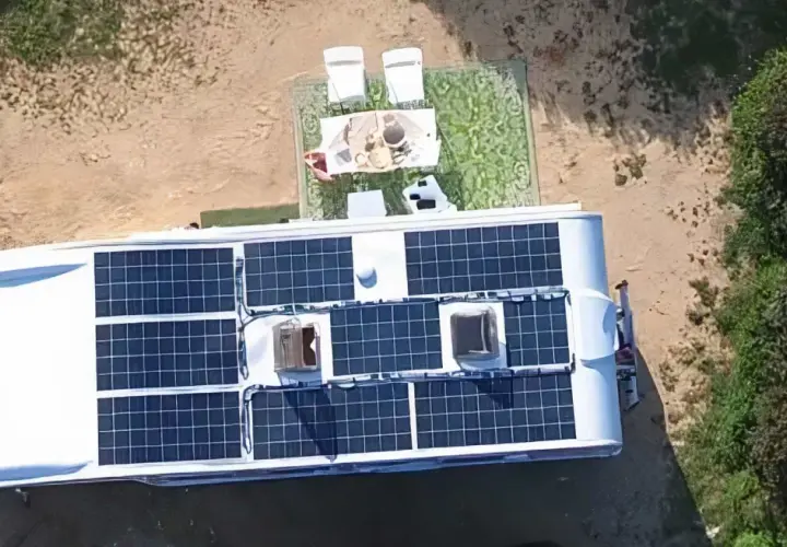 Kamper z panelami słonecznymi na dachu, idealny do życia w stylu instalacja off grid. Na zewnątrz stolik z kawą i krzesła.