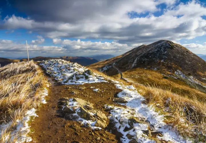 Szlak przez Bieszczady na Ukrainę, pokryty pierwszym śniegiem i jesienną trawą, pod burzowym niebem.