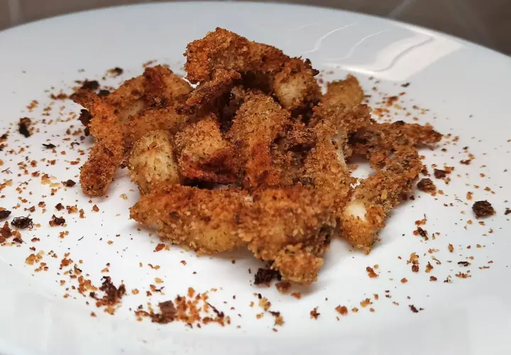 Un mucchietto di seppie gratinate al forno, dorate e croccanti, su un piatto bianco.