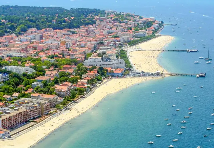 Vue aérienne d'une ville côtière avec une plage bondée et des bateaux dans l'eau.