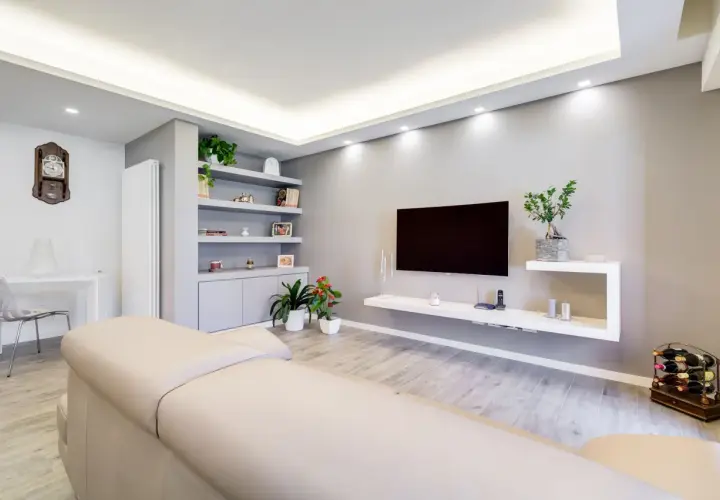Mobile TV in cartongesso, con mensole e vani contenitori integrati. Soggiorno moderno con divano chiaro e pavimento effetto legno.