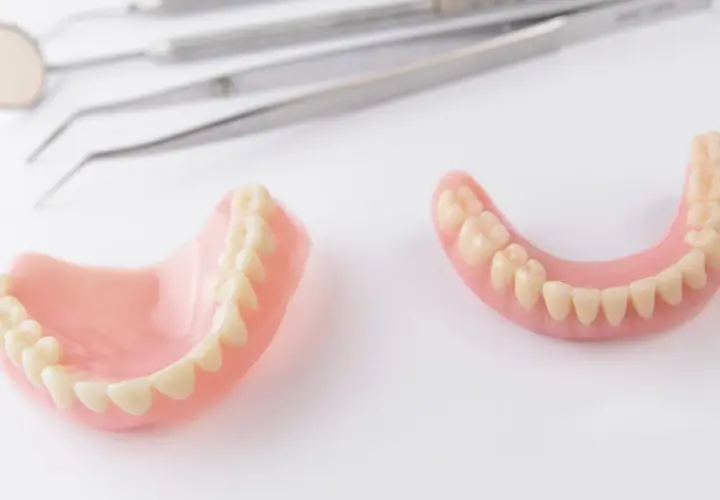 Protesi dentarie, superiori e inferiori, su sfondo bianco, con strumenti dentistici sfocati sullo sfondo. Soluzione per denti mobili.