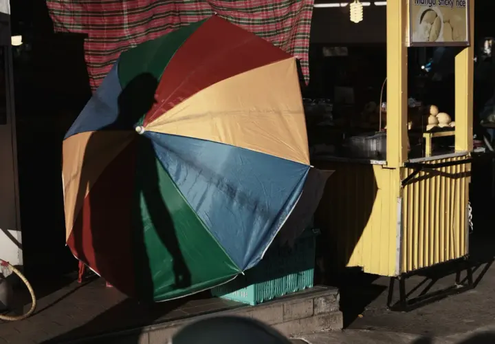 Kolorowy parasol rzuca cień na uliczny stragan z mango sticky rice. Fotografia miejska.