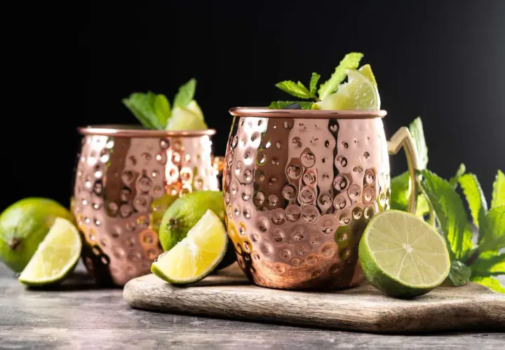 Due tazze di rame martellato per un Moscow Mule, guarnite con menta fresca e spicchi di lime.