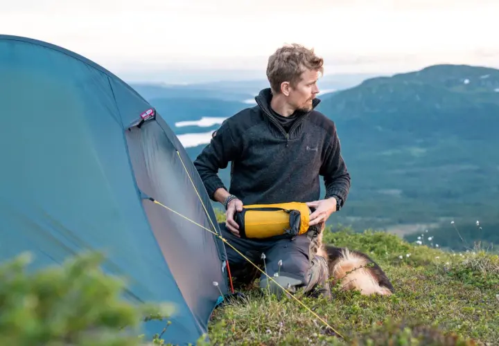 Man med hund förbereder tältet för en vintervandring i fjällen.
