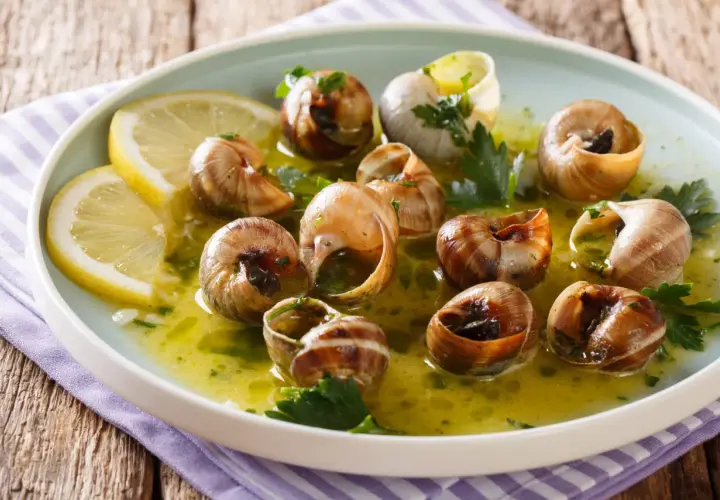 Escargot to danie z gotowanych ślimaków w sosie czosnkowo-ziołowym, podane z plasterkami cytryny.