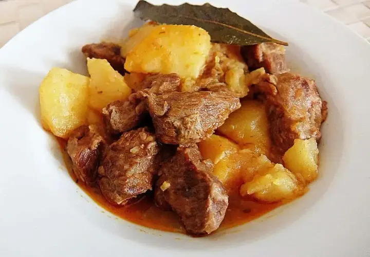 Sabroso morcillo de ternera guisado con patatas y una hoja de laurel, servido en un plato blanco.