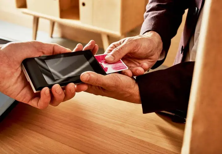 Dwie dłonie zbliżają kartę do terminala płatniczego. To prosty sposób, jak doładować telefon na kartę.