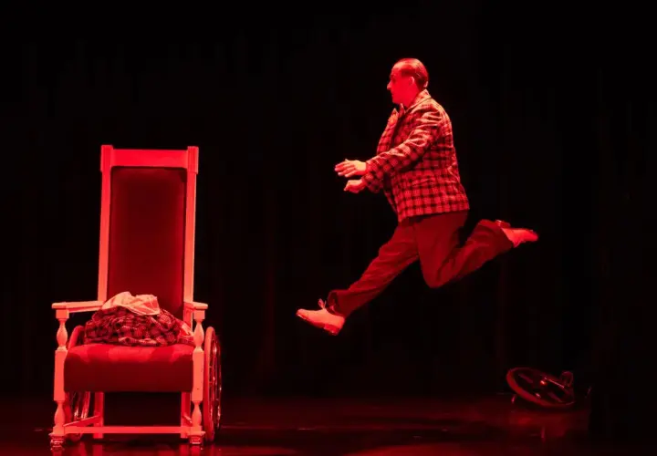 Aktor w skoku na scenie Teatru Komedia Kraków. Czerwone światło podkreśla dynamikę sceny.