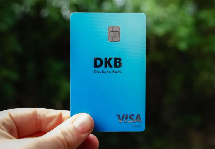 Eine blaue DKB Visa Debitkarte wird in der Hand gehalten, mit unscharfem Grün im Hintergrund.