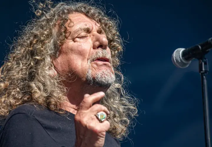 Wokalista Led Zeppelin, Robert Plant, śpiewa do mikrofonu, z charakterystyczną burzą kręconych włosów.