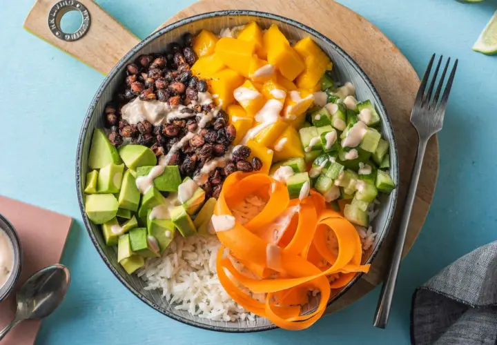 En färgglad poke bowl med ris, svarta bönor, mango, gurka, avokado och morotsstrimlor, toppad med en krämig dressing.