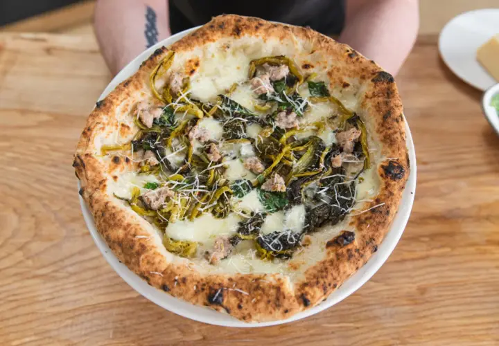 Pizza mit Salsiccia und Friarielli, belegt mit geschmolzenem Käse und geriebenem Parmesan.