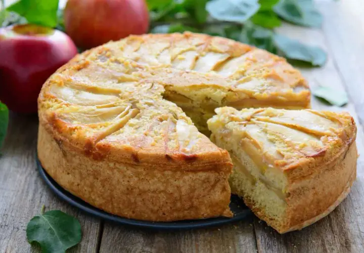 Deliziosa torta di mele vegana con fette di mela disposte a raggiera sulla superficie dorata. Una fetta è già stata servita.
