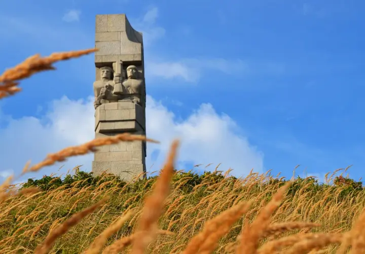 Pomnik Obrońców Wybrzeża na Westerplatte podczas zwiedzania. W oddali widać dwie kamienne postacie żołnierzy.