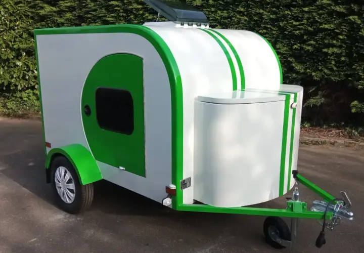 Caravane blanche et verte au design unique, rappelant une goutte d'eau. Parfaite pour des escapades écologiques.
