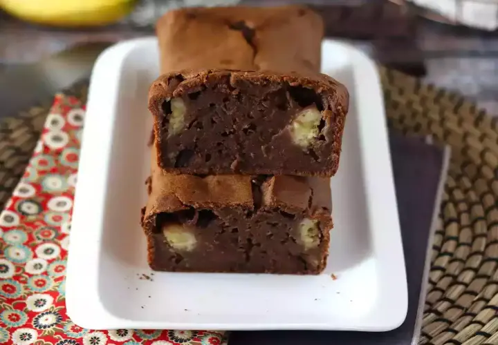 Dos porciones de bizcocho de plátano y chocolate apiladas, con trozos de plátano visibles en su interior.