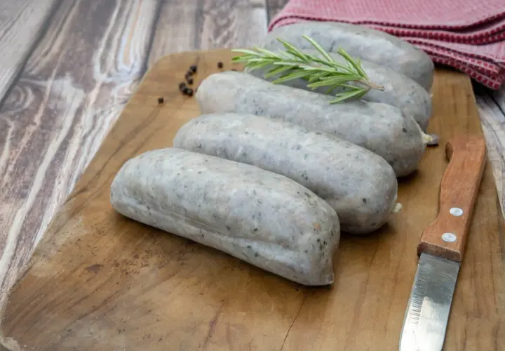 Saucisses grises sur planche en bois, avec romarin et poivre. La différence entre andouille et andouillette est subtile, mais la texture ici suggère une andouillette.