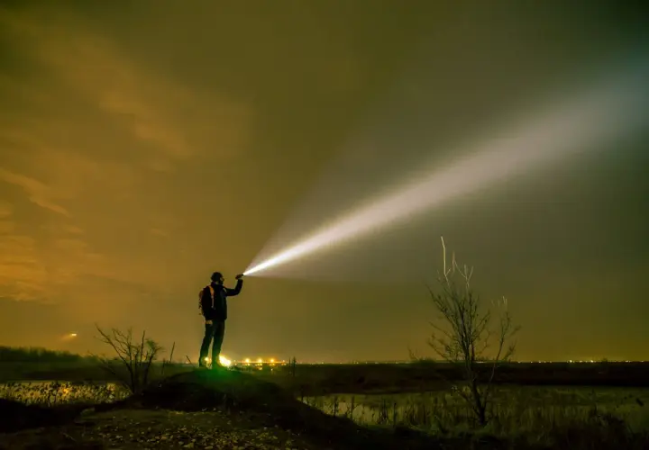 Mężczyzna z plecakiem oświetla nocne niebo potężnym snopem światła z latarki o dużym zasięgu.