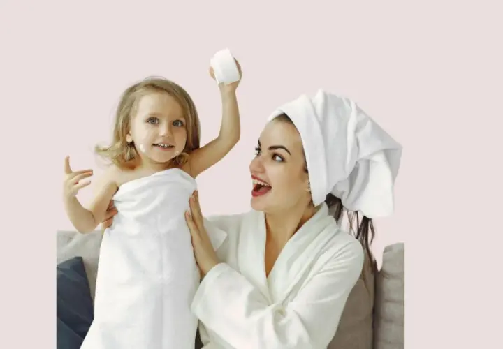 Mère et fille profitent d'un moment de **soin du visage pour petite fille fait maison**. La petite est enroulée dans une serviette, avec de la crème sur le nez.