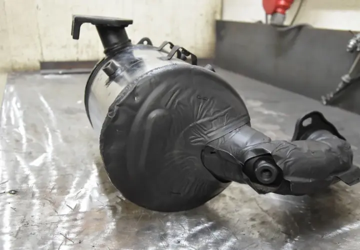 Filtr cząstek stałych DPF owinięty czarną taśmą na metalowym stole.