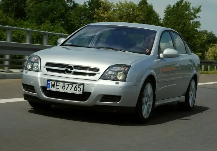 Srebrny Opel Vectra C GTS pędzi po drodze, otoczony zielenią.