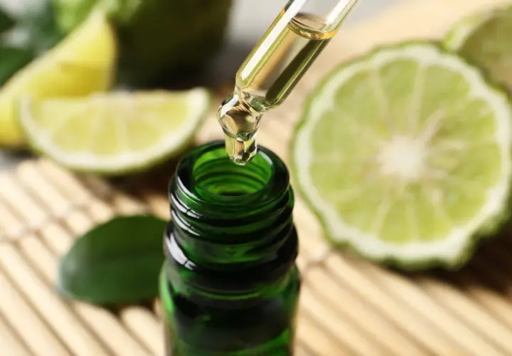 Une goutte d'huile essentielle de bergamote tombe d'une pipette dans un flacon vert. Un remède de grand-mère pour lutter contre la fatigue, entouré de fruits coupés.