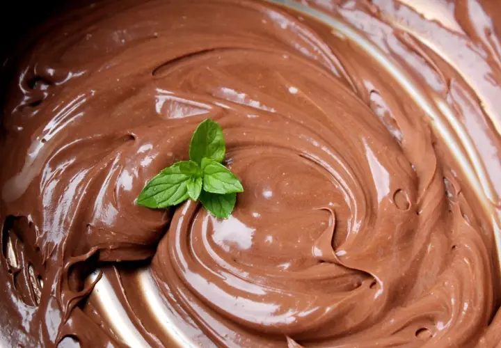 Una fogliolina di menta fresca adorna una spirale di lucida ganache al cioccolato, invitando a un assaggio goloso.