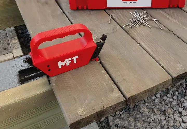 Röd MFT-apparat för att skruva trall dolt. En hög med skruv ligger redo.