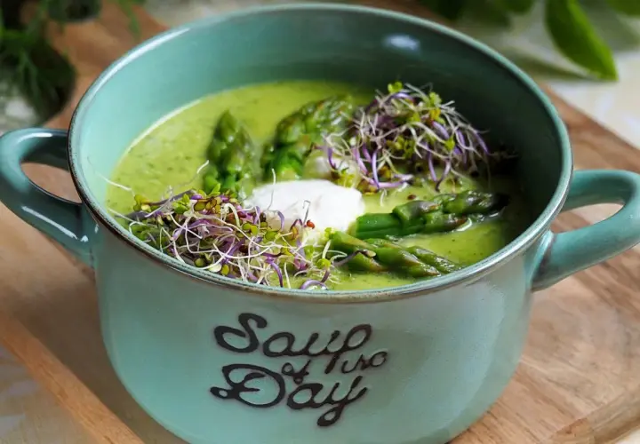 Aksamitna zupa z zielonych szparagów, udekorowana kiełkami i kleksem śmietany, w ceramicznej misce z napisem "Soup of the Day".