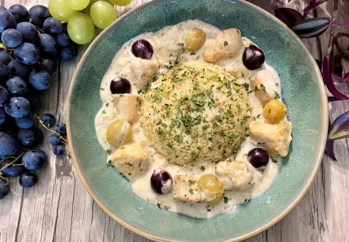 Un délicieux poulet au raisin crémeux, servi avec du riz et garni de persil frais. Des grappes de raisins noirs et verts complètent cette assiette appétissante.