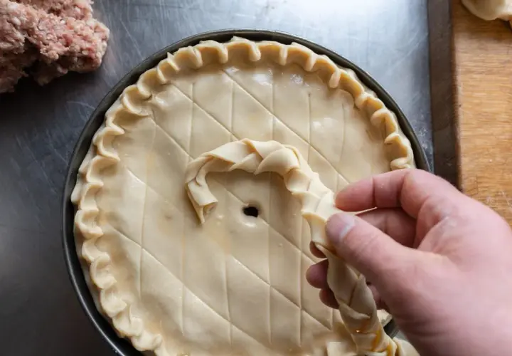 Préparation d'une tarte salée, peut-être une recette joue de porc rapide. Une pâte est décorée avec une tresse.