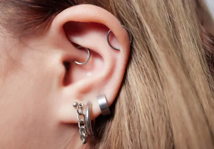 Ucho z kilkoma kolczykami, w tym daith piercing z małym kółkiem.