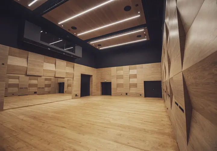 Nowoczesna sala prób w Teatrze Ludowym w Krakowie. Drewniane ściany i podłoga, lustra i oświetlenie tworzą inspirującą przestrzeń.