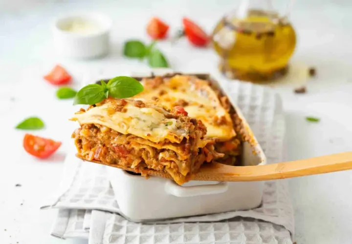 Une part généreuse de lasagne, digne d'une recette de chef italien, est servie. Tomates et basilic frais décorent ce plat réconfortant.