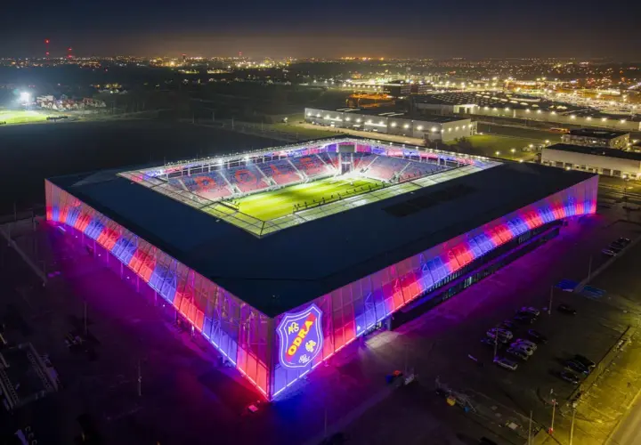 Nowoczesny stadion Odra Opole nocą, oświetlony na czerwono i niebiesko.