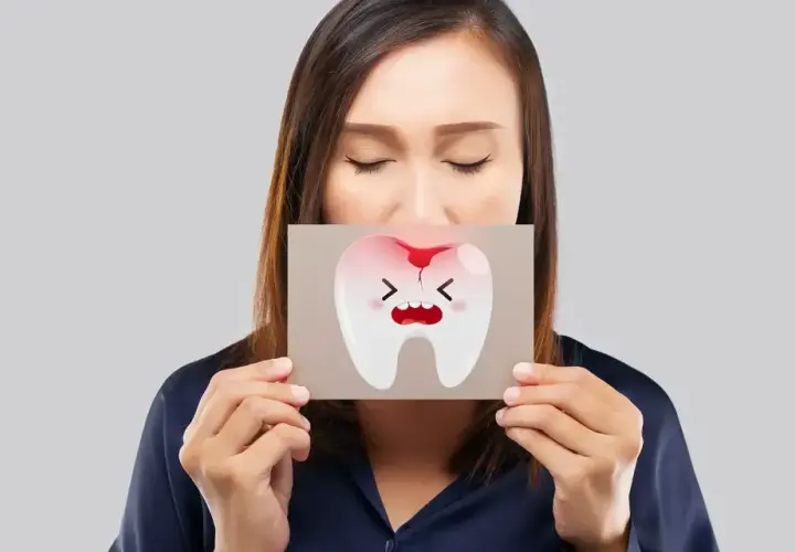 Donna con gli occhi chiusi mostra un disegno di un dente che cade, con espressione sofferente e macchie di sangue.