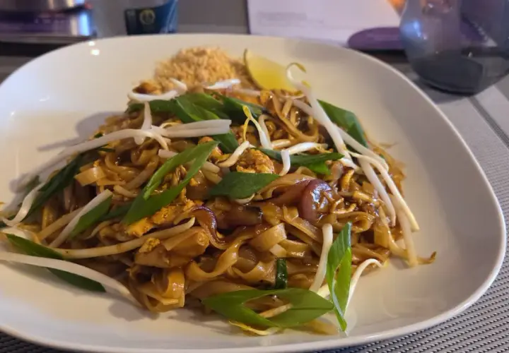 Pad thai z kurczakiem, kiełkami fasoli mung, szczypiorkiem i ćwiartką limonki na białym talerzu.