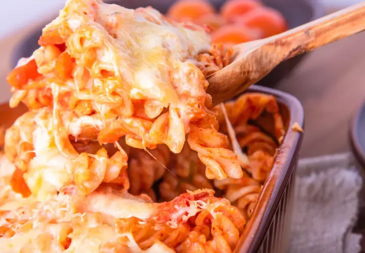 Un cucchiaio solleva un'abbondante porzione di pasta alla sorrentina filante, con pomodoro e mozzarella dorata.