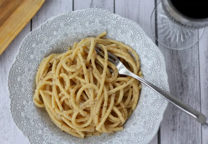 Porcja pysznego cacio e pepe na ozdobnym talerzu, z widelcem w makaronie.