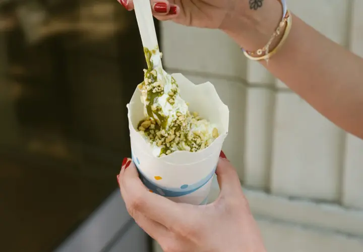 Ręce trzymają kubek z lodami mcflurry pistacjowe, posypane orzeszkami i polane zielonym sosem.