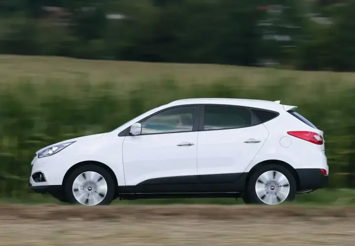 Biały Hyundai ix35 2.0 benzyna w ruchu, z rozmytym tłem zielonych pól i drzew.
