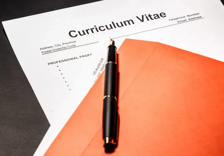 Eleganckie pióro na tle dokumentu Curriculum Vitae po angielsku i pomarańczowej koperty.