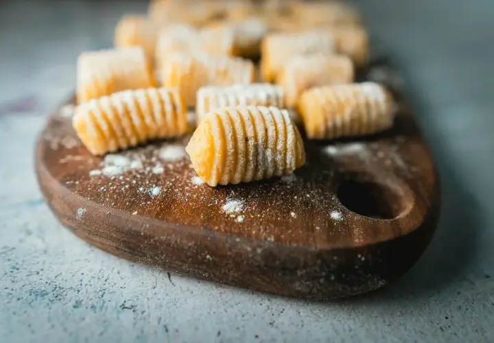 Gnocchi di patate fatti in casa, pronti per essere cucinati, disposti su un tagliere di legno scuro.