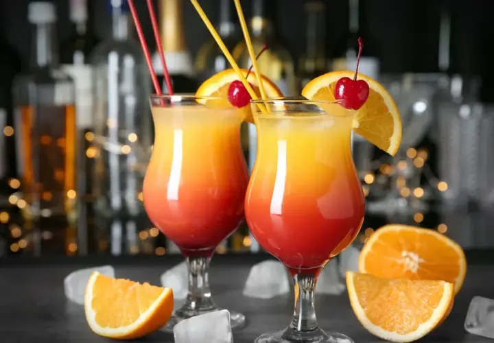 Dwa drinki z wódką czystą, ozdobione pomarańczą i wiśnią, z kostkami lodu i owocami w tle.