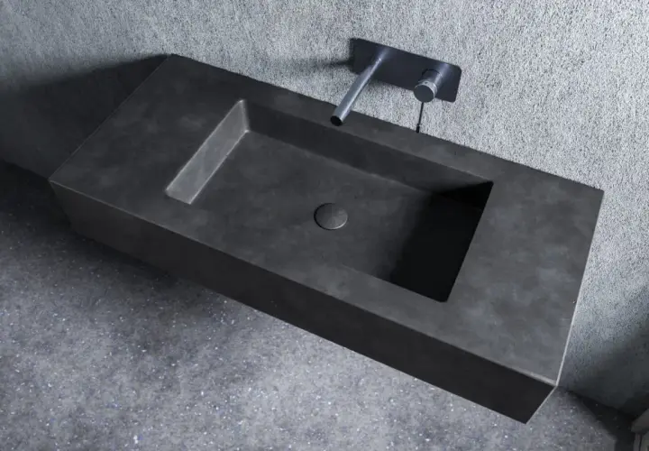 Nowoczesna umywalka z betonu o minimalistycznym designie, z wpuszczonym w blat odpływem i elegancką baterią ścienną.