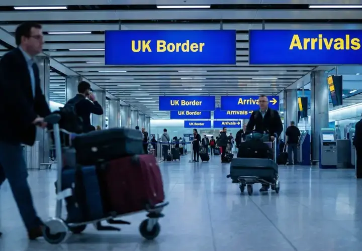 Ludzie z bagażami przechodzą przez lotnisko w Wielkiej Brytanii, kierując się do UK Border i Przylotów.